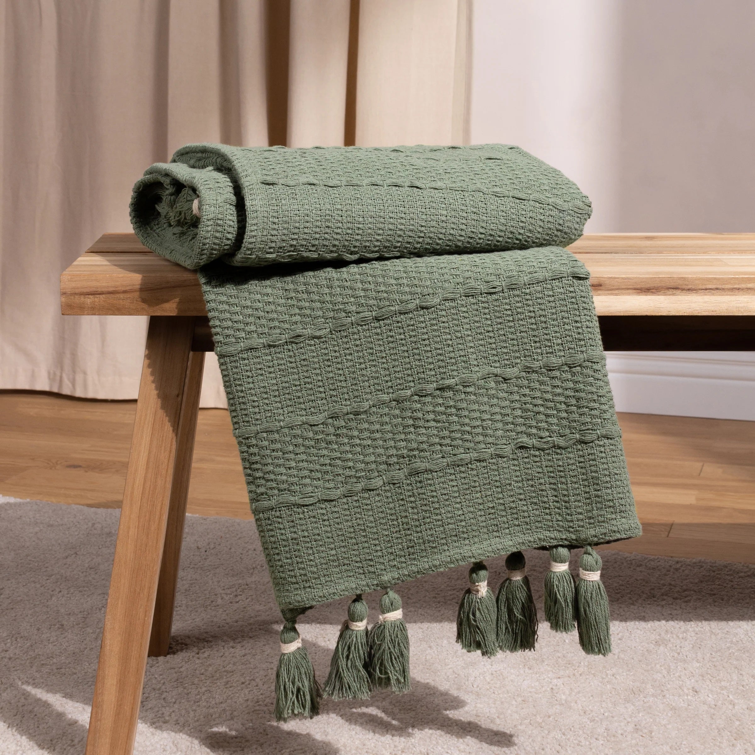 Green textured throw blanket with tassels on a wooden table