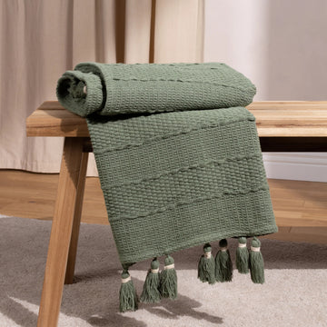 Green textured throw blanket with tassels on a wooden table