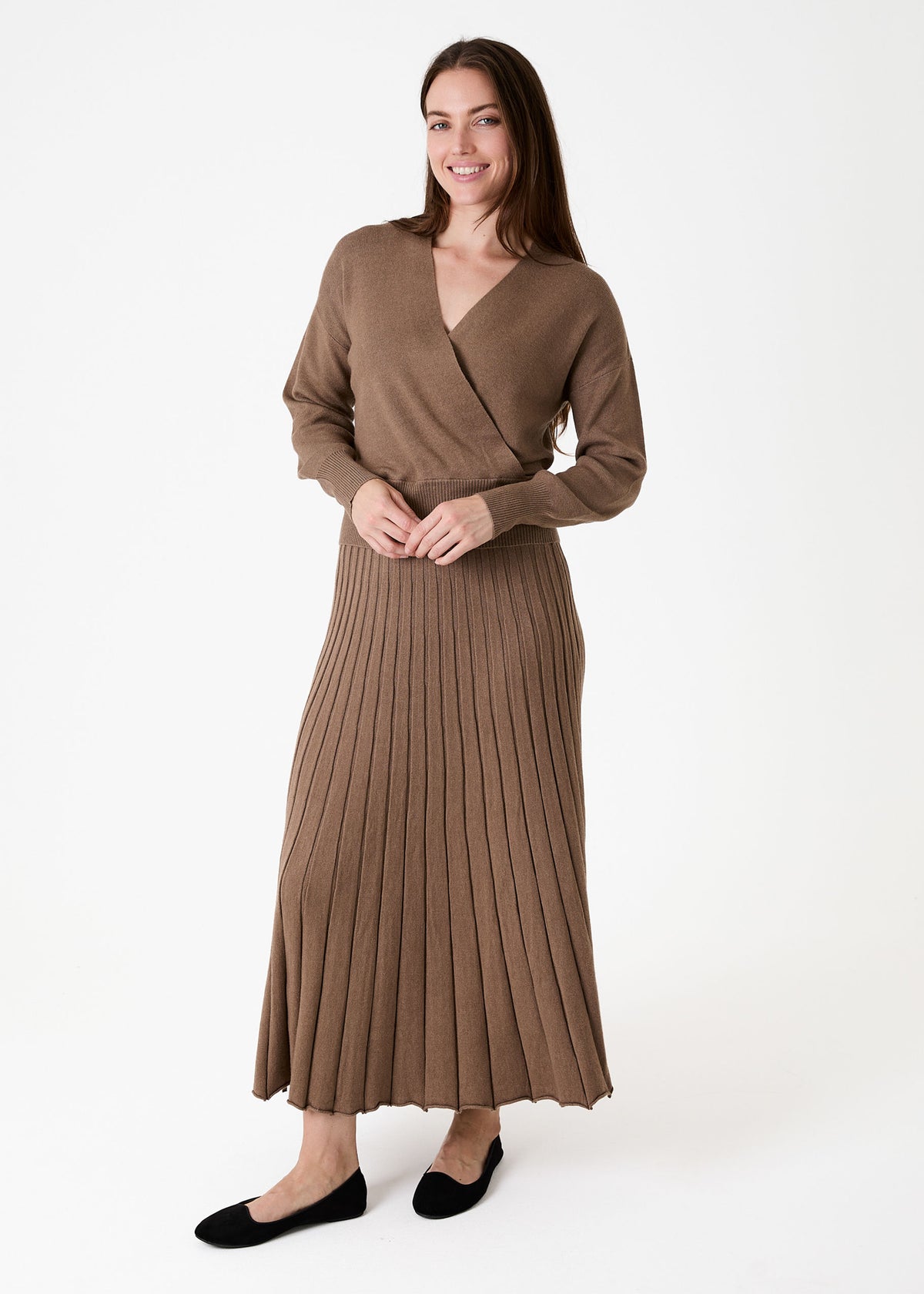 Cashmere Like Pleated Skirt Mink. A woman modeling a brown long-sleeve wrap-style top and matching pleated midi skirt set, paired with black flats, against a plain white studio background.