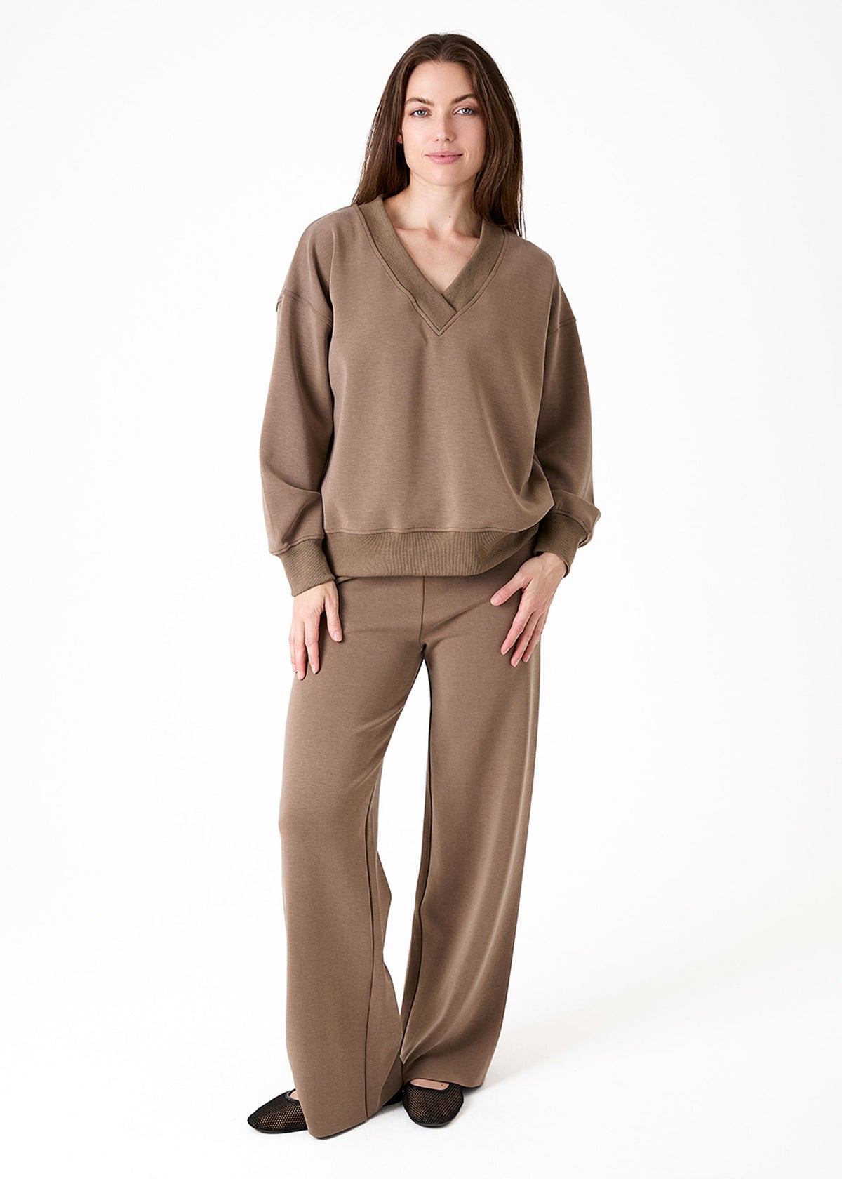 A woman modeling a matching taupe brown loungewear set consisting of a V-neck long-sleeve sweatshirt and wide-leg pants, photographed against a seamless white studio background.