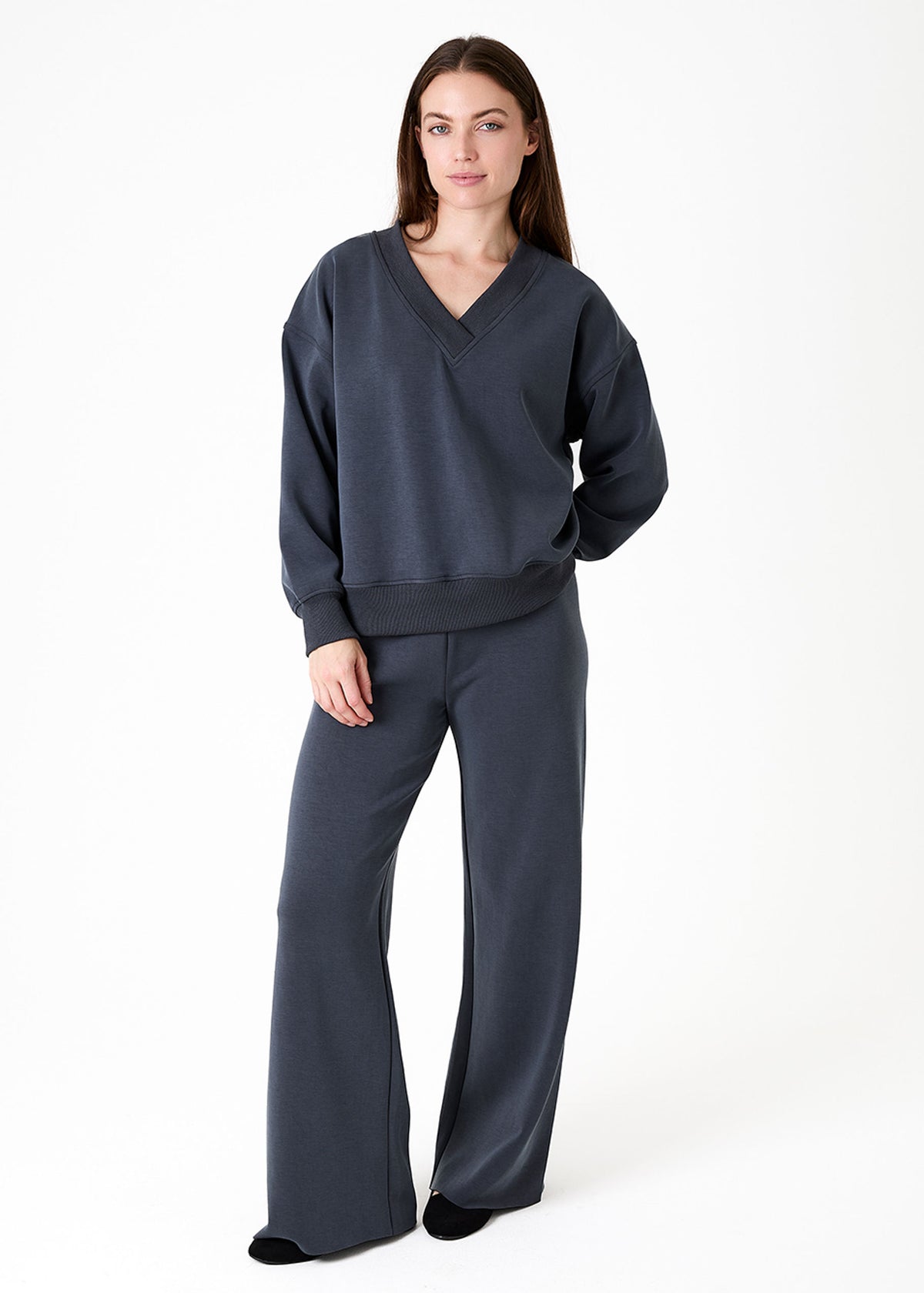Luxe Jersey Straight Leg Trouser Slate Grey. A woman modelling a dark slate grey lounge set consisting of a V-neck sweatshirt and matching wide-leg pants, photographed against a clean white studio background.